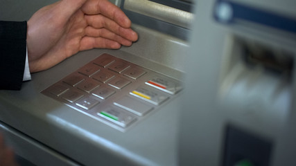 Wall Mural - Man hiding keyboard of automated teller machine while inserting his pin code