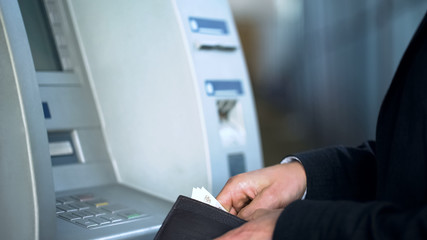 Wall Mural - Male hands putting banknotes in purse, withdrawing money from bank account, ATM