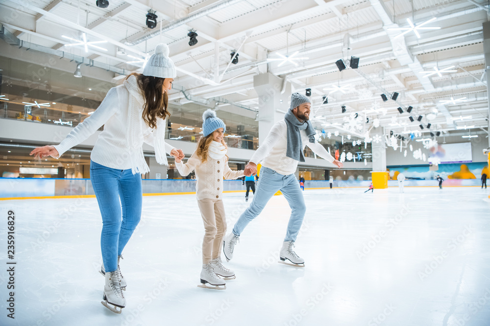 smiling family holding hands while skating together on ice rink - obrazy, fototapety, plakaty 