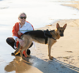 Happy attractive senior woman with her german shepard dog playing on the beach at autumn sunset