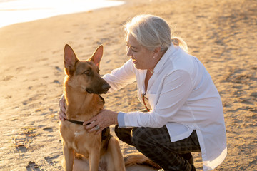 Portrait o happy attractive senior woman with her german shepard dog on the beach at autumn sunset