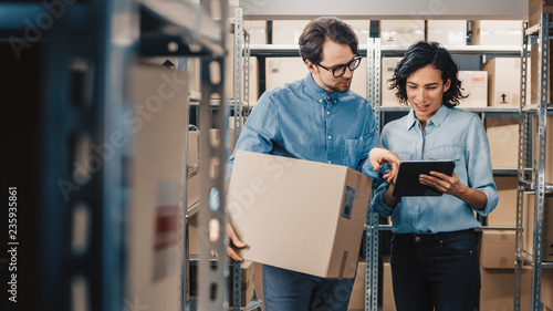 Fotomural Female Inventory Manager Shows Digital Tablet Information to a Worker Holding Cardboard Box, They Talk and Do Work