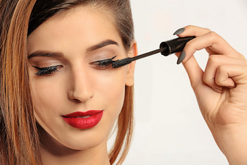 Wall Mural - Woman applying mascara on her eyelashes against white background