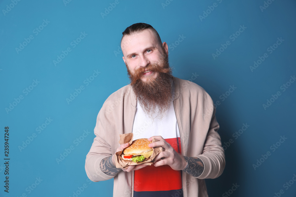 Bearded man with yummy burger against color background