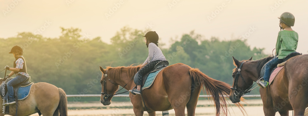 Kids learn to ride a horse near the river before sunset. - obrazy, fototapety, plakaty 