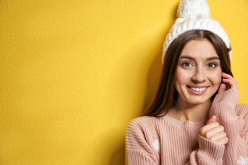 Sticker - Beautiful young woman in warm sweater with hat on color background. Space for text