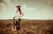 gorgeous cowgirl with old guitar standing at rural meadow