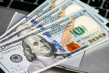 Closeup view of one hundred dollar banknotes lying on the laptop keyboard.