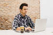 © ADDICTIVE STOCK - Young man using laptop at table with cup and smartphone