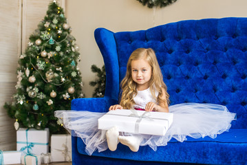 little girl sitting near the Christmas tree with a New Year's gift