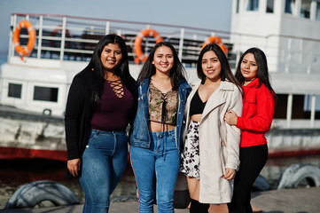 Wall Mural - Group of four happy and pretty latino girls from Ecuador posed against boat.