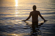 © lazyllama - Sunrise silhouette of man standing in calm ocean waters facing the golden morning sun