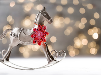 Christmas silver vintage horse with red wooden snowflake on neck against festive bokeh background, new year celebration greeting card, copy space