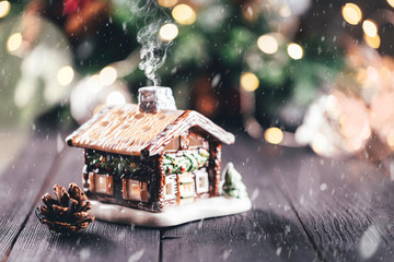 Christmas village house with candle inside on rustic table with christmas tree in the background, bokeh lights, snow and smoke effect, copy space