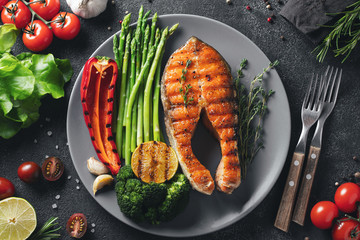 Tasty and healthy salmon steak with asparagus, broccoli and red pepper on a gray plate. Diet food on a dark background. Top view. Flat lay