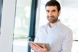 © Sergey Nivens - Young handsome businessman using his touchpad standing in office