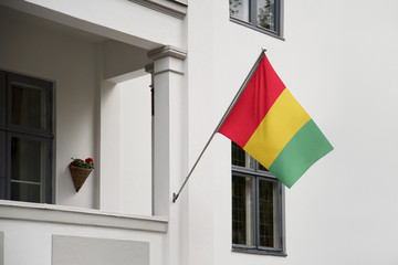 Wall Mural - Guinea flag hanging on a pole in front of the house. National flag waving on a home displaying on a pole on a front door of a building and raised at a full staff.
