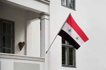 Wall Mural - Syria flag hanging on a pole in front of the house. National flag waving on a home displaying on a pole on a front door of a building and raised at a full staff.