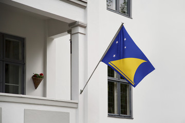 Wall Mural - Tokelau flag hanging on a pole in front of the house. National flag waving on a home displaying on a pole on a front door of a building and raised at a full staff.