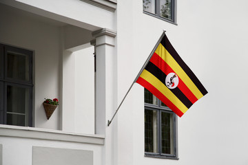 Wall Mural - Uganda flag hanging on a pole in front of the house. National flag waving on a home displaying on a pole on a front door of a building and raised at a full staff.