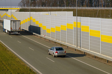 Truck and passenger car moving along the highway protected by sound barriers.