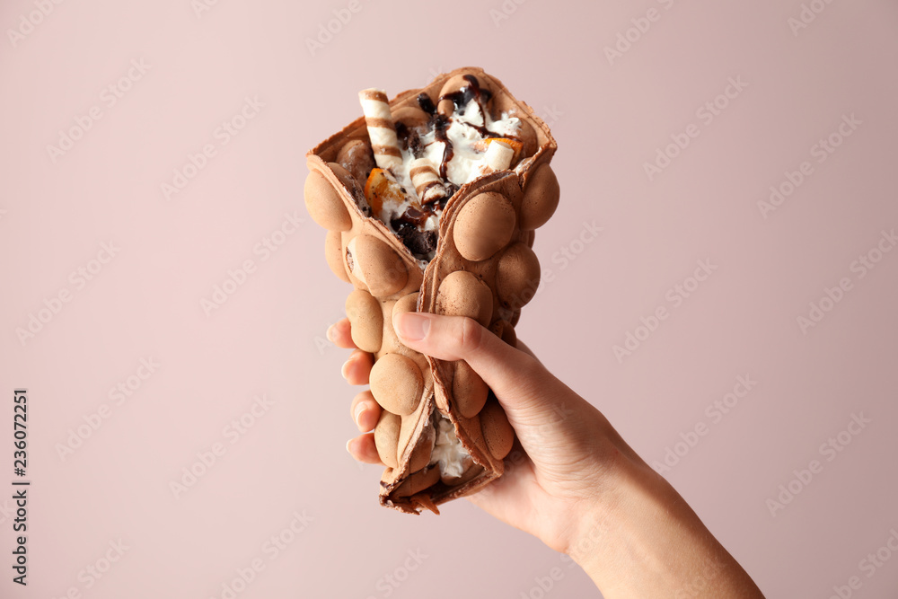 Female hand with delicious sweet bubble waffle on color background