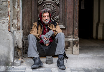 Wall Mural - Homeless beggar man sitting outdoors in city asking for money donation.