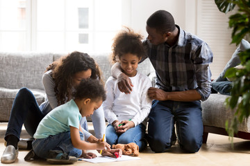 Wall Mural - Large African American family playing together on warm floor in living room, mother help toddler son with drawing, loving father embracing little preschooler daughter, family spending time together