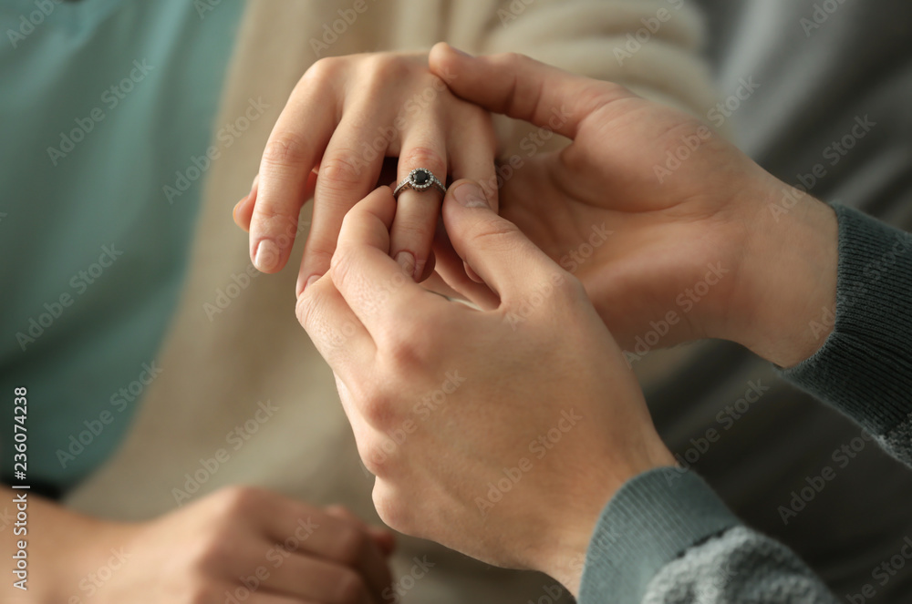 Young man putting engagement ring on fiancee's finger, closeup