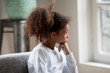 Thoughtful serious African American preschooler girl looking in window, pensive child sitting at home, hold hands under chin, dreaming, looking in distance, feeling boredom, having questions