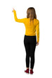 © luismolinero - A full-length shot of a young girl with yellow sweater pointing back with the index finger on isolated white background