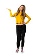 © luismolinero - A full-length shot of a young girl with yellow sweater holding copyspace imaginary on the palm to insert an ad on isolated white background