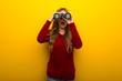 © luismolinero - Young girl on vibrant yellow background and looking in the distance with binoculars