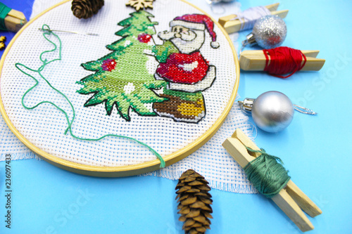 Picture embroidered with a cross child, preparing for the New Year and  Christmas. Christmas tree green, Santaklaus of thread. Accessories and  tools for embroidery. Festive mood, holiday. - Buy this stock photo