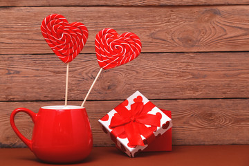 Heart shaped Lollipop in red Valentine's day mug on wooden background. Greeting card.