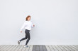 © bodnarphoto - Happy girl wearing sportswear running against the background of a white wall. Young attractive woman is running on the street on a white background. Copyspace