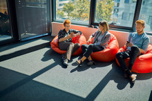 Colleagues With Cell Phones Sitting In Bean Bags In Office Lounge