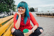 © Westend61 - Portrait of smiling young woman with dyed blue hair sitting on a bench with beverage