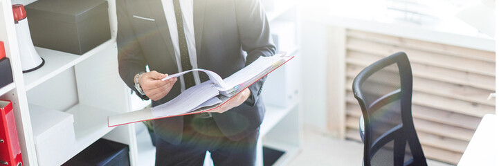 Wall Mural - The man is standing near the rack in the office and scrolls through the folder with the documents.