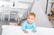 © LIGHTFIELD STUDIOS - cute toddler boy standing near bed, smiling and looking at camera in apartment