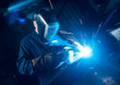 A vibrant action shot of a skilled working metal welder in action, welding metal. Photographed with a slow shutter speed and spark trails. Orange and teal.