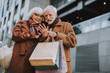 © Yakobchuk Olena - Portrait of stylish lady holding smartphone while husband with shopping bags pointing at display. They watching videos and smiling