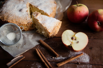 Homemade pie with apples and cinnamon sticks on wooden background.