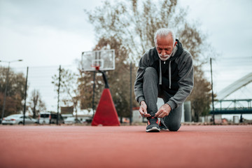 Low angle image of senior runner tying shoelaces before a run on stadium.