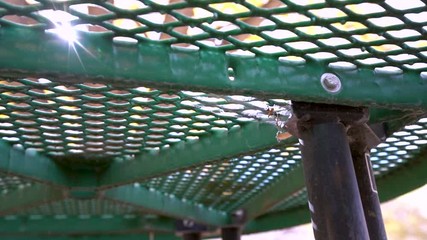 Slow motion shot of dirty spider web waving in the wind under picnic table with sun shining through