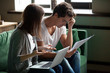 © fizkes - Millennial stressed young couple sitting on sofa at home and checking unpaid bills, taxes, due debt, bank account balance. Bankruptcy, debt and lack of money, financial problems in family concept