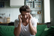 © fizkes - Young attractive stressed overworked person sitting on sofa with closed eyes touch head, having head ache or high blood pressure at home. Health problems or hangover after yesterdays hangouts, party