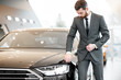 © rh2010 - Portrait of an elegant businessman touching headlight of a luxury car in the showroom
