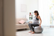 © New Africa - Young pregnant woman in fitness clothes sitting on exercise ball at home. Space for text