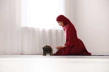 Wall Mural - Muslim woman in hijab praying on mat indoors